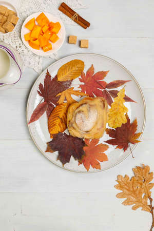 Autumn concept. Pumpkin cinnabon on a plate, colorful autumn leaves and spices on the table. Overhead on a light gray background.の写真素材