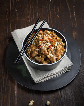 Chinese cuisine, a dish from Sichuan province. A popular dish is Kung pao, pieces of chicken fillet in a sauce with peanuts and hot chili pepper. Close-up on a dark wooden background, verticalの写真素材