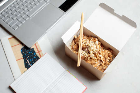 Lunch break in the office, lunch box with chicken in hot sauce on the desktop with laptop, diary. Close-up.の写真素材
