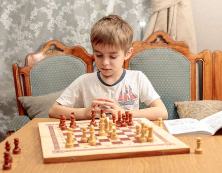 Teaching children chess. A blond boy reflects on a chess example from a textbook
