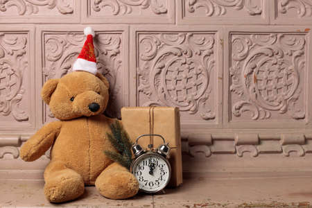 The concept of winter holidays.Antique mantelpiece with a teddy bear, alarm clock, fir branches and a gift box. Horizontal, with spaceの写真素材