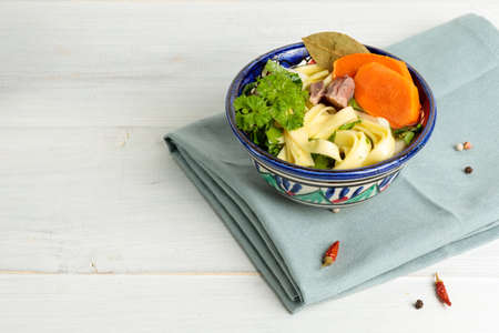 Homemade noodles with vegetables and meat. In a brightly painted bowl. Close-up, on a light wooden background, horizontal with spaceの写真素材