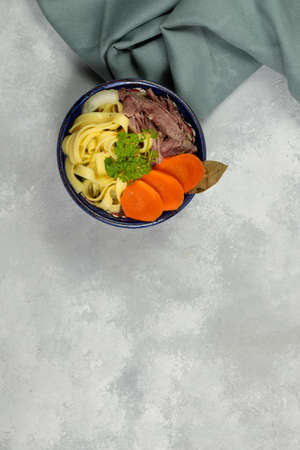 Homemade noodles, with broth, boiled meat and vegetables. Top view on a gray background, a copy of the spaceの写真素材