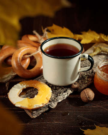 Hot tea in an enameled cup, a bunch of bagels with butter and honey on a dark wooden background. Low key, selective focus.の写真素材