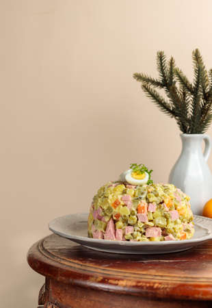 Olivier salad on a plate, on a round wooden vintage table. Spruce branches in a vase in the background. Vertical, with spaceの写真素材