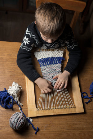 A child weaves a rug made of knitted threads on a homemade loom. Top view. Recycling of old clothes