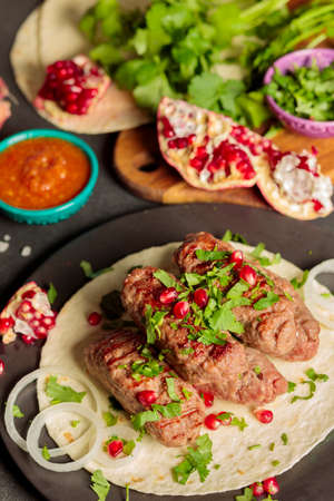 Kebabs on the pit, with coriander greens, onions and pomegranate seeds. Close-up, ingredients in the...