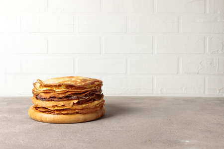 A stack of thin pancakes on a round wooden tray. Horizontal, on a light brick background, with space