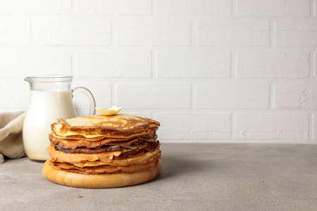A stack of thin pancakes on a wooden plate and a jug of milk. Close-up, horizontal, copy of the spaceの写真素材