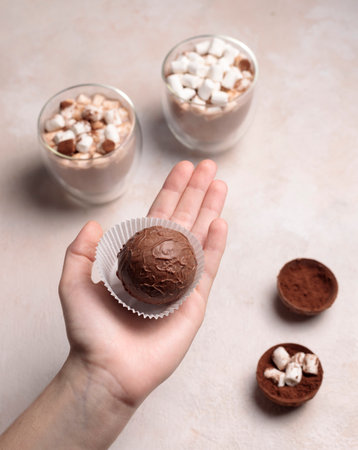 Chocolate bombs with cocoa and marshmallows for making a hot aromatic drink. The hand holds a chocolate ball. Glasses of cocoa in the background.の写真素材