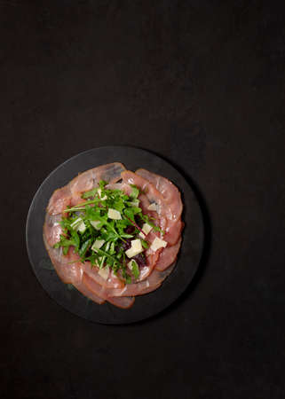 Carpaccio, with salad leaves, parmesan and dressing. On a black background, vertical with spaceの写真素材
