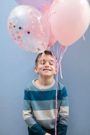 a smiling boy holds a bouquet of balloons. Vertical frame on a blue background.の写真素材