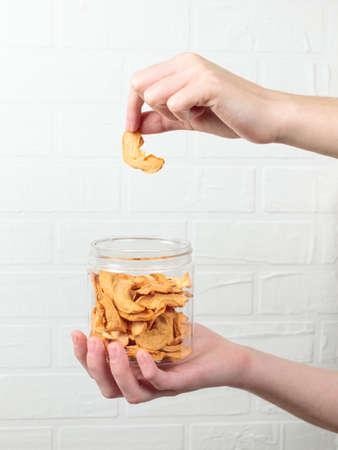 Hands holding a transparent plastic container with dried apples, in one hand a slice of apple.の写真素材