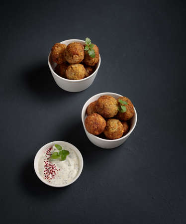 Snack, street food. Falafel, cheese balls or meatballs in two small bowls and white sauce. On a...