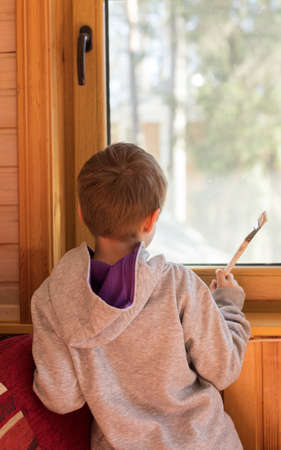 A child with a brush in his hands looks out of the window of the cottage.の写真素材