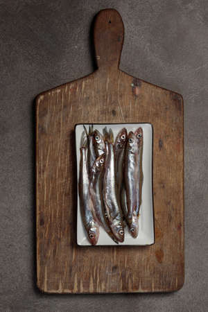 Small raw fish on a chopping board. Top view on brown backgroundの写真素材