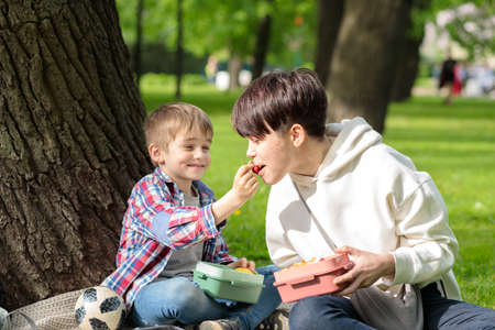 A young woman with her younger brother on a picnic in the park eating berries from a container