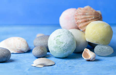 Japanese mochi desserts or ice cream balls, close-up on a blue background with shells and sea...