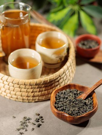 Green tea in a glass teapot and two Japanese porcelain cups on a wicker tray. Close-upの写真素材