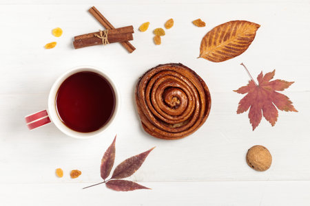 Autumn layout with dry leaves, a hot drink in a cup and a bun with raisins.の写真素材