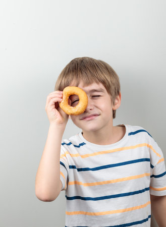 The blond boy looks through the donut as if through a monocle. Portrait on a light background.の写真素材