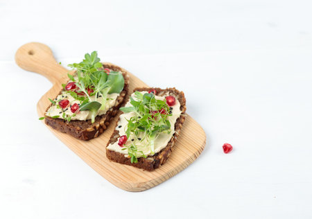 Sandwich with hummus, micro greenery and pomegranate seeds on a wooden board. Close-up on a light background.の写真素材