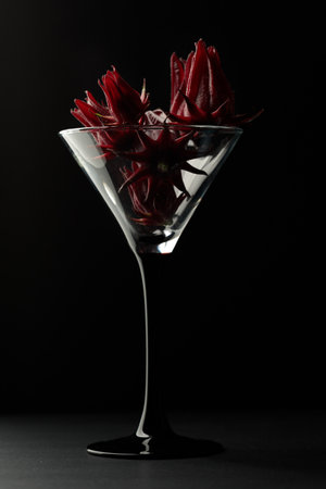 Cocktail glass filled with hibiscus flowers. Black background, vertical.の写真素材