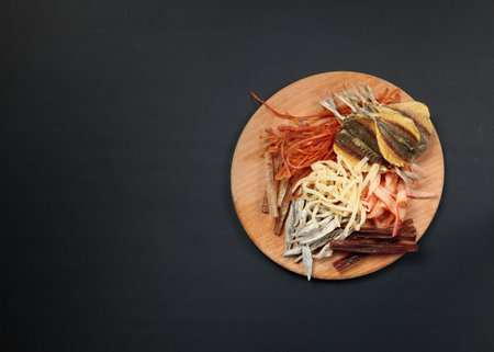 Snack board with dried and salted fish and squid. Top view on black background, copy space.