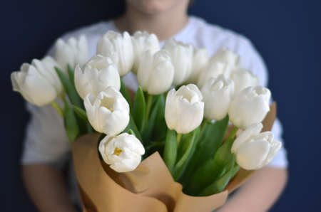 A person holding a bouquet of white tulips wrapped in craft paper. Navy blue backround