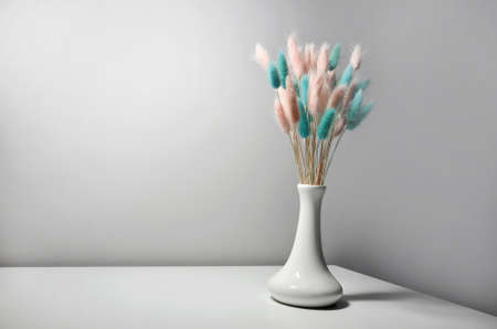 Beautiful bouquet of pink and blue lagurus in a white vase standing on a white tableの写真素材
