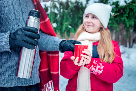 Man gives hot tea to his daughter in winter forestの写真素材