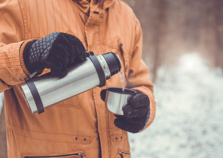Man pours tea out of bottle. Winter forest. Close-upの写真素材