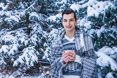 Young woman holds cup of coffee with marshmallow in winter forestの写真素材