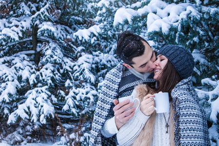 Couple kisses and drinks coffee with marshmallow in winter forestの写真素材