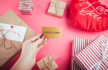 Buying presents for Valentines day with a gold card. Gift boxes and heart pillow on pink backgroundの写真素材