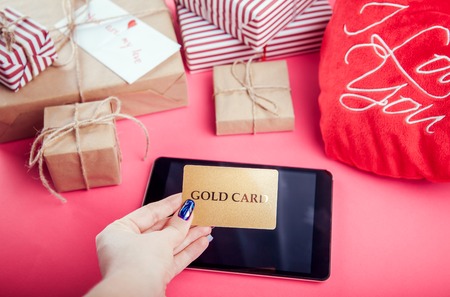 Buying presents for Valentines day with a gold card. Gift boxes and heart pillow on pink backgroundの写真素材