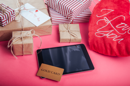 Buying presents for Valentines day with a gold card. Gift boxes and heart pillow on pink backgroundの写真素材