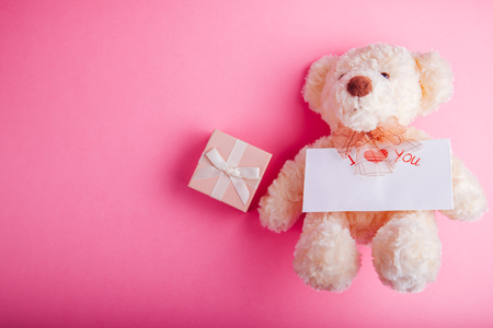 Teddy bear with a gift box and a card for Valentines day on pink backgroundの写真素材