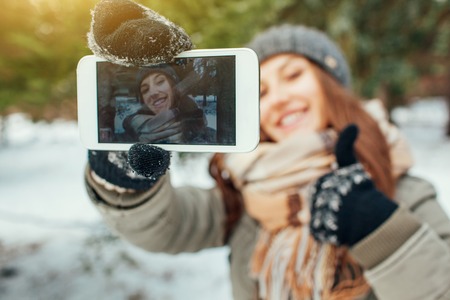 Young woman takes selfie in winter forest with her smartphone