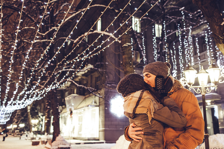Young couple in love kisses under holiday winter illumination at nightの写真素材
