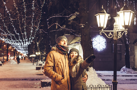 Young couple walking in winter city center under holiday illumination at nightの写真素材
