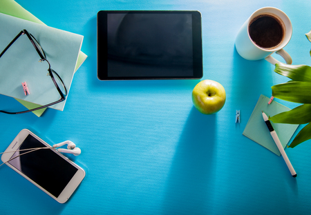 Workspace of a creative office employee. Working with a cup of coffee, using a phone and tablet on blue backgroundの写真素材