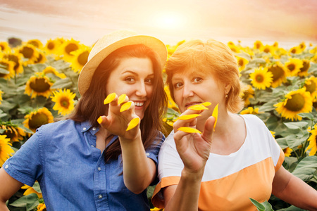 Middle-aged mother and her daughter having fun in sunflower field at sunsetの写真素材