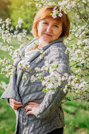Middle-aged woman walks in spring garden among blooming treesの写真素材