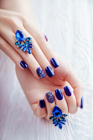 Blue manicure with earrings on white wooden backgroundの写真素材