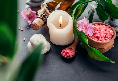Spa essentials including candle, salt, stones, oil and green leaves on black backgroundの写真素材