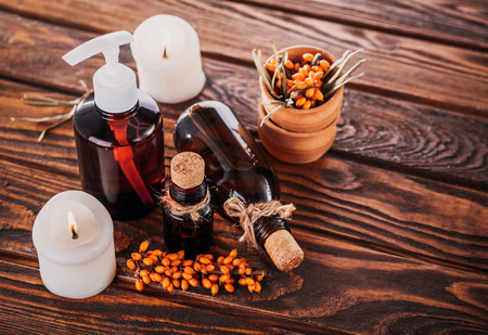 Spa essentials including sea buckthorn, lemon and ginger oils and candles on wooden background. Organic cosmetics conceptの写真素材