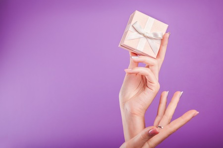 Female hands with beautiful manicure holding a small gift box on violet background.の写真素材