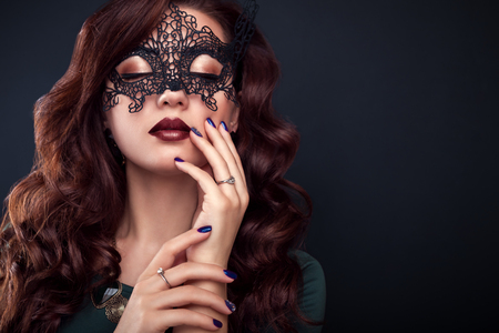 Beautiful woman with perfect make-up and manicure wearing a lace mask on black backgroundの写真素材