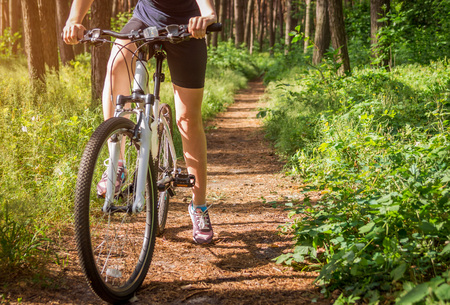 Young woman riding a bicycle in the forest at sunsetの写真素材